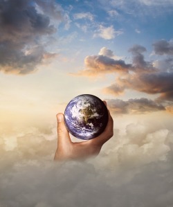 Globe of earth held in a hand in a background of clouds.
